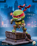 Sculptor's render of the painted design (kit ships unpainted): three-quarter front view of the red-masked chibi turtle crouched with two sais on the rooftop vent unit, duct pipe and pavement base, against a snowy night city